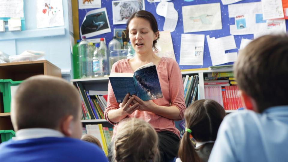 Una mujer le lee un libro a un grupo de niños. 