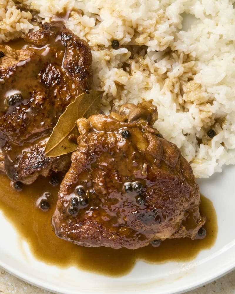 Two chicken thighs prepared in Filipino adobo on a plate with rice on the side.