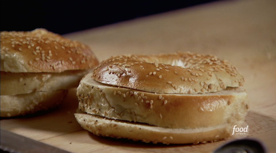 Two sesame seed bagels on a wooden surface sliced into thirds