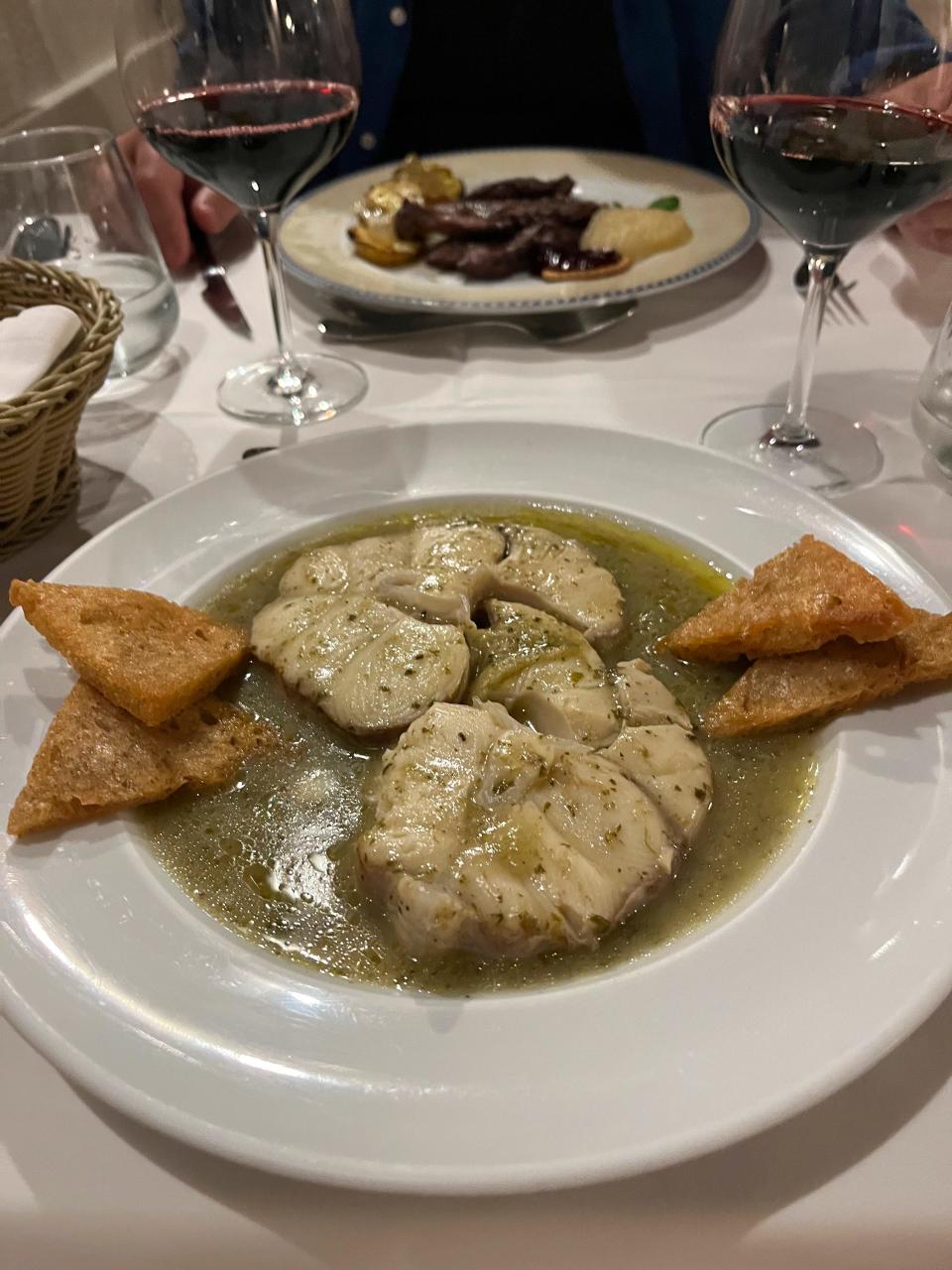 Traditional Alentejan dishes, dogfish in coriander sauce, foreground, and medallions of local black pork, smashed apples and roasted potatoes are served at Restaurante Fialho in Évora, Portugal on Sept. 20, 2023. (Kristen de Groot via AP)