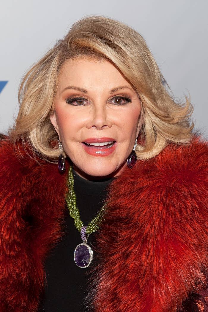 Joan Rivers in a fur coat with a purple pendant, and purple earrings at a celebrity event