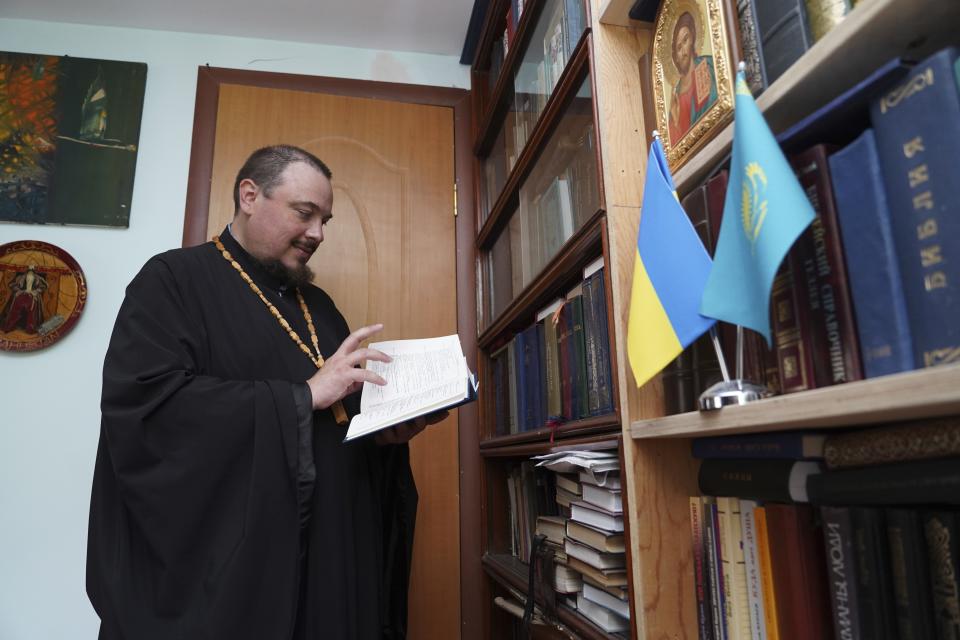 The Rev. Iakov Vorontsov leafs through a book with Ukraine's and Kazakhstan's national flags on the right, in his apartment in Almaty, Kazakhstan, on Wednesday, Aug. 9, 2023. Vorontsov, a priest in Kazakhstan, was shocked and desperate when he first heard that Russia sent troops into Ukraine. He was hoping the church would step in to mediate the conflict. But his calls to preach peace received no support: his superiors reassigned him several times, forbade him from giving sermons, and told parishioners to stay away from him. In the end, Vorontsov decided to temporarily stop serving. (Vladimir Tretyakov/NUR.KZ via AP)