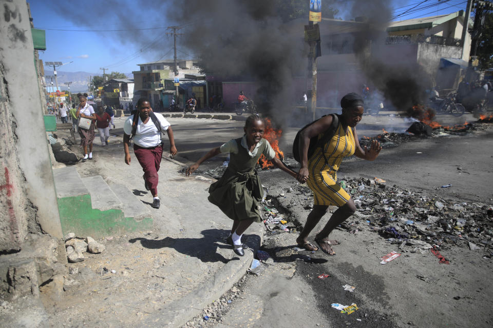 FILE - A woman and her daughter run past a barricade that was set up by police protesting bad police governance in Port-au-Prince, Haiti, Jan. 26, 2023. Haiti's latest crisis entered full throttle following the 2021 assassination of President Jovenel Moïse, when current Prime Minister Ariel Henry emerged in a power struggle as the country’s leader and the country's nearly 200 gangs have taken advantage of the chaos, warring for control. (AP Photo/Odelyn Joseph, File)