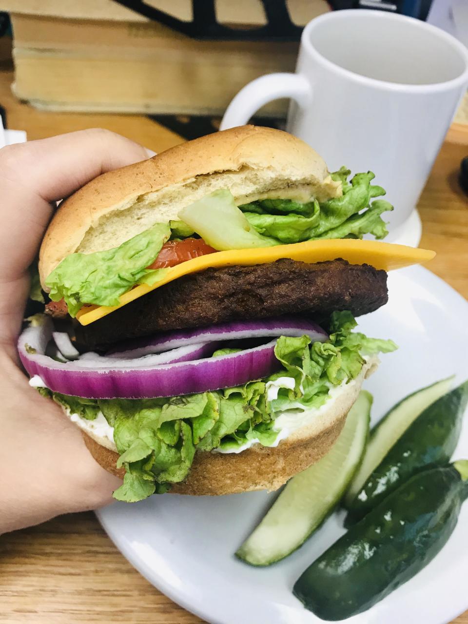 holding up a veggie burger on a plate with pickles