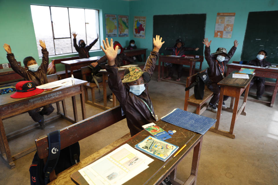 Aymaran Indigenous students raise their hands as they wear new, protective uniforms during the first week back to in-person classes amid the COVID-19 pandemic, near Jesus de Machaca, Bolivia, Thursday, Feb. 4, 2021. (AP Photo/Juan Karita)