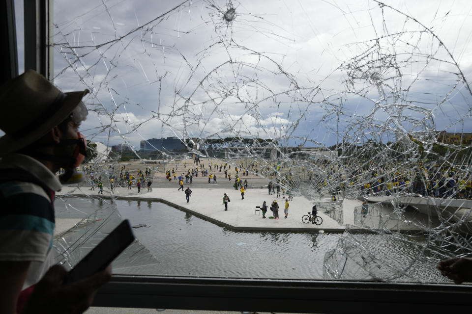 FILE - A protester, supporter of Brazil's former President Jair Bolsonaro, looks out from a shattered window of the Planalto Palace after he and many others stormed it, in Brasilia, Brazil, Sunday, Jan. 8, 2023. Planalto is the official workplace of the president of Brazil. (AP Photo/Eraldo Peres, File)