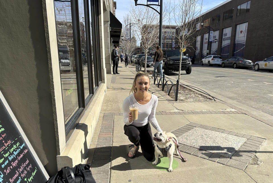 Erin Hooker, 29, and her French bulldog, Ella, took advantage of the unseasonably warm weather on Monday, Feb. 26, 2024, with a lunchtime walk in Des Moines, Iowa, and Hooker's first iced coffee of the season. (AP Photo/Hannah Fingerhut)