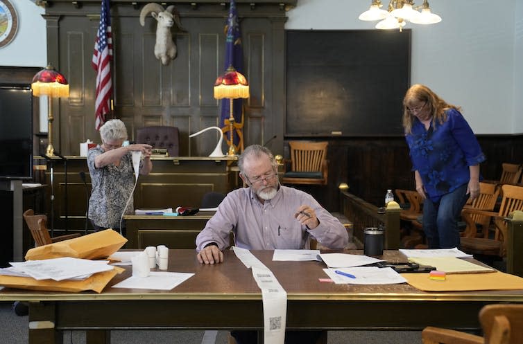 A person sits at a table with a long strip of paper running over the edge toward the floor.