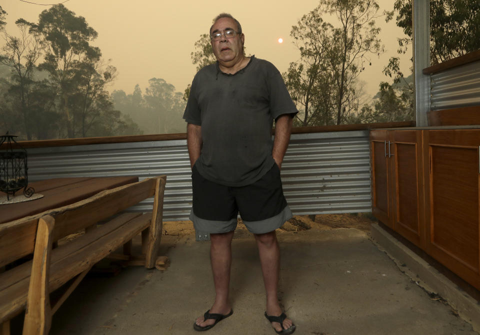 In this Jan, 11, 2020, photo, Joe Elvaro stands on the back deck his house at Burragate, Australia a day after an anticipated wildfire impact failed to come. It seemed imminent to those hunkering at the fire station that "The Beast" would finally roar through. But on this night the wildfire only crept closer, prodding forward a few tentative fingers before going dormant again as the winds died. (AP Photo/Rick Rycroft)