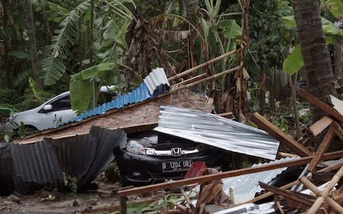 Cars are covered by debris at an area ravaged by a tsunami in Carita, Indonesia - Credit: AP