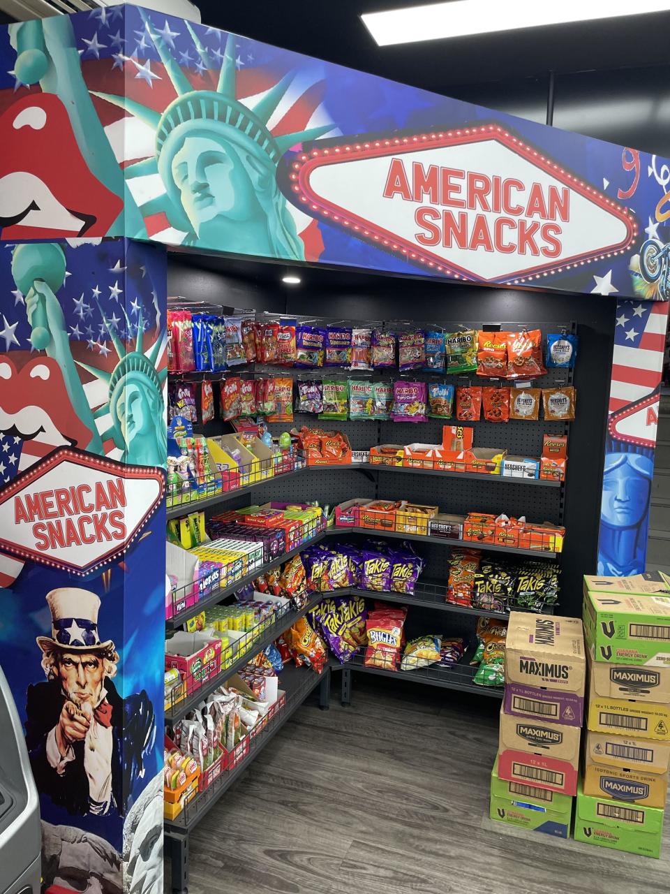 American snack display with various packaged snacks like chips and candies, featuring Uncle Sam and Statue of Liberty art on the shelving