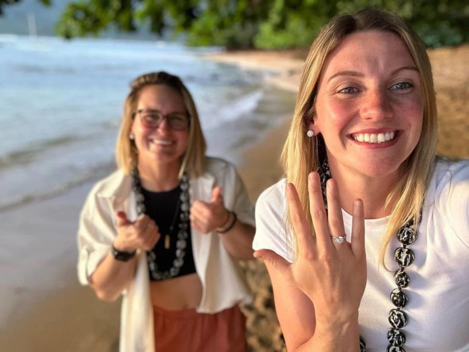 Marie-Philip Poulin, left, and Laura Stacey, who are teammates on the Canadian women's national hockey team, are seen showing off their engagement rings on a beach in Hawaii. (@pou29/Instagram - image credit)