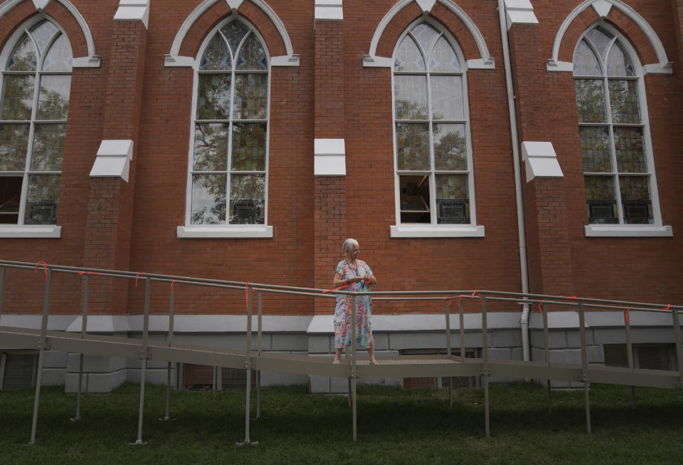 Anna Beaulieu ties orange ribbons to the handicap railing outside of Sacred Heart Church of the First Peoples to symbolize the Indigenous children forced to attend and assimilate into residential schools in Canada, on Sunday, July 17, 2022, in Edmonton, Alberta. Pope Francis will meet with parishioners at Sacred Heart during his visit to the Canadian province. (AP Photo/Jessie Wardarski)