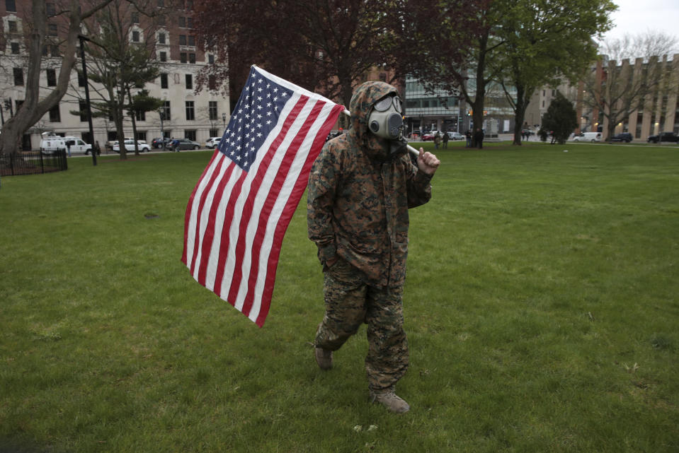 A protester carries an American flag while wearing a gas mask during a rally at the State Capitol in Lansing, Mich., Thursday, May 14, 2020. People angry over Michigan's coronavirus stay-at-home order protested outside the state Capitol on Thursday, braving heavy rain to call for business owners to reopen in defiance of Gov. Gretchen Whitmer. (AP Photo/Paul Sancya)