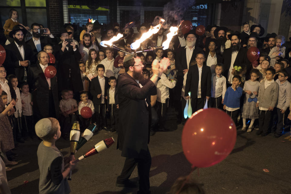 FILE - In this Oct. 18, 2016, file photo, a performer wears lighted sticks on his head while entertaining a crowd during the Jewish holiday of Sukkot, celebrated by the Chabad Lubavitch community in Brooklyn's Crown Heights neighborhood, in New York. For years, ultra-Orthodox Jewish families pushed out of increasingly expensive Brooklyn neighborhoods have been turning to the suburbs, where they have taken advantage of open space and cheaper housing to establish modern-day versions of the European shtetls where their ancestors lived for centuries before the Holocaust. (AP Photo/Mark Lennihan, File)