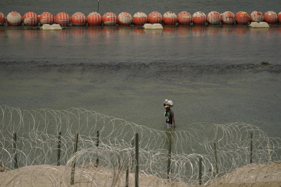 A migrant from Columbia walks along Concertina wire and a floating buoy barrier after crossing the Rio Grande from Mexico into the U.S., Monday, Aug. 21, 2023, in Eagle Pass, Texas. (AP Photo/Eric Gay)