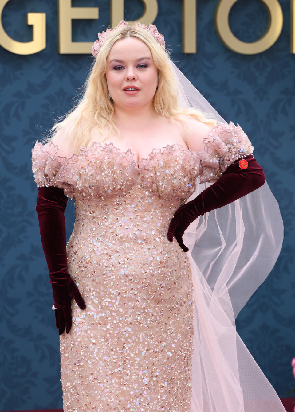 Nicola Coughlan at a red carpet event, wearing an off-shoulder, sequined gown with sheer details and long velvet gloves