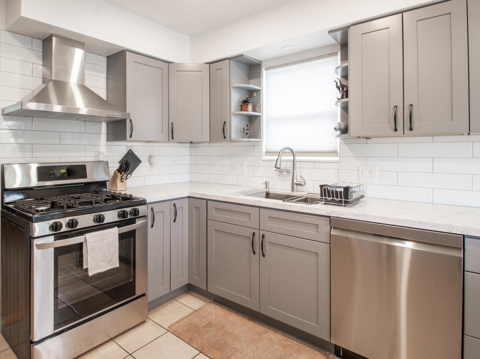 Stainless steel stove, dishwasher, and range hood in a gray kitchen with white subway tile