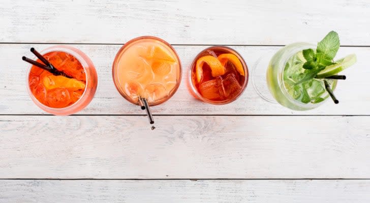 An overhead photo of four cocktails in a row on a white-painted wooden table.