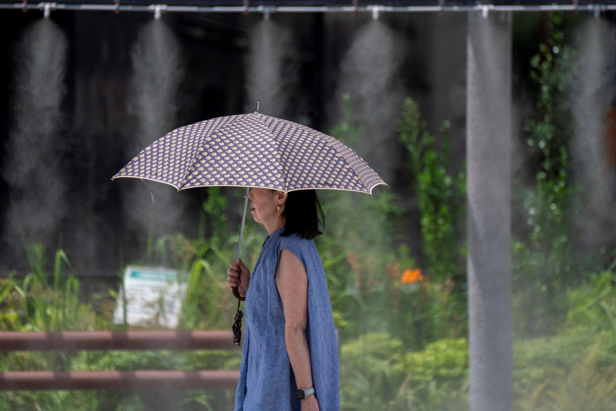 A woman holding an umbrella over her head walks past a mist shower during hot weather.