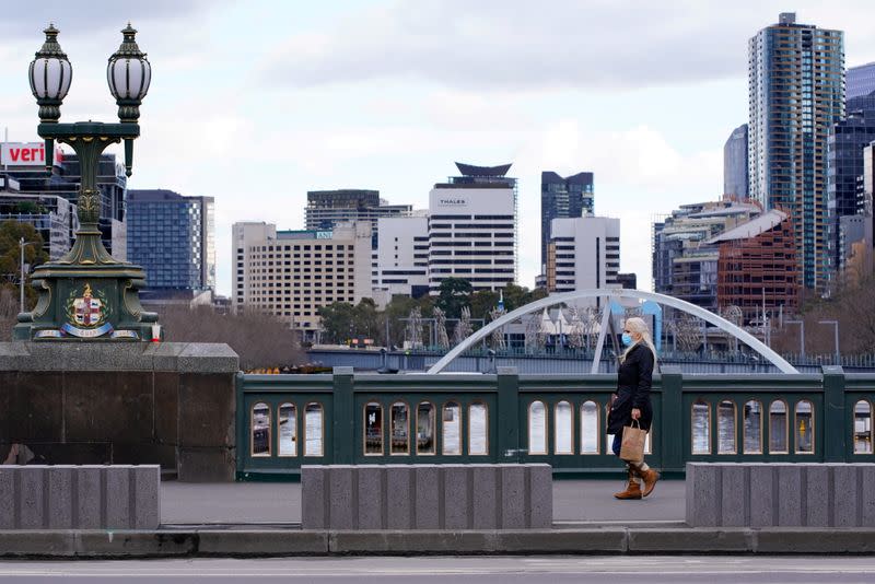 FILE PHOTO: A lone woman, wearing a protective face mask, walks across a city centre bridge a in Melbourne