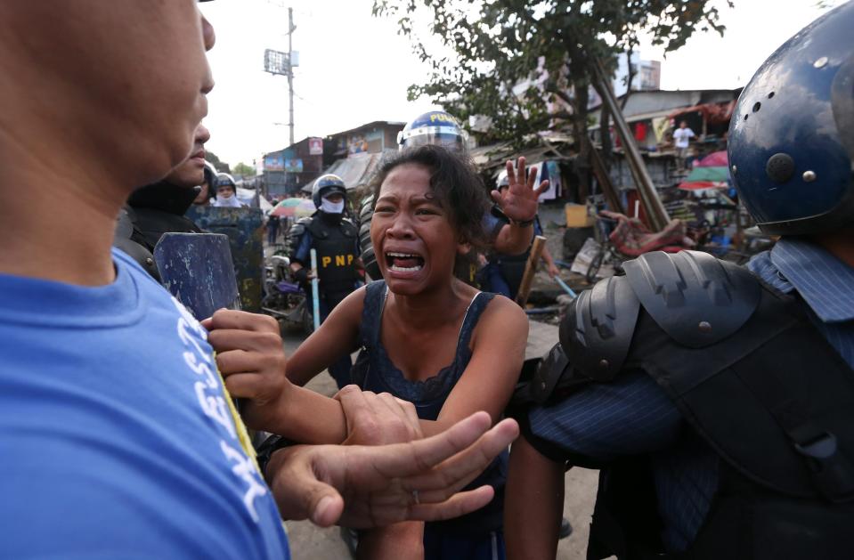 epa04044222 A Filipino woman cries as she tries to prevent a policeman from arresting her father during a demolition of shanties at Sitio San Roque in Quezon City, east of Manila, Philippines, 27 January 2014. Throwing rocks, pillboxes, and even human waste, illegal settlers barricaded the demolition team in Baranggay Bagong Pag-asa. Four residents were arrested and twelve were reported injured. Residents report receiving cash from 300 to 450 US dollar in exchange for their voluntary relocation. Earlier, hundreds of the urban poor marched to the city hall in protest of the demolition that will pave the way for the rise of a business district. EPA/DENNIS M. SABANGAN