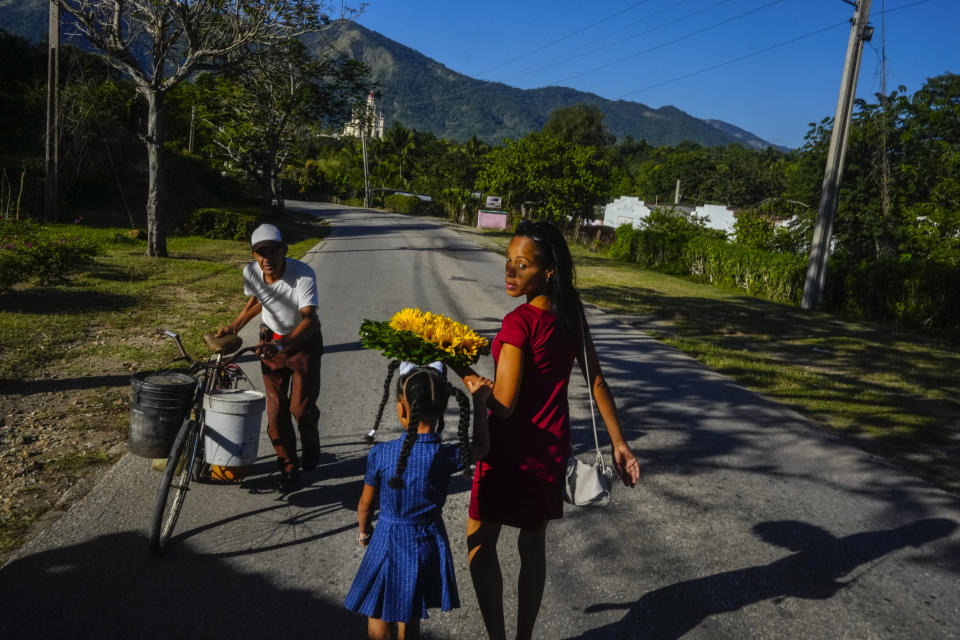 Dainet Cala and her daughter Evelyn carry flowers to leave as an offering at the shrine of the Virgin of Charity of Cobre in El Cobre, Cuba, Sunday, Feb. 11, 2024. The Vatican-recognized Virgin, venerated by Catholics and followers of Afro-Cuban Santeria traditions, is at the heart of Cuban identity, uniting compatriots from the Communist-run Caribbean island to those who were exiled or emigrated to the U.S. (AP Photo/Ramon Espinosa)