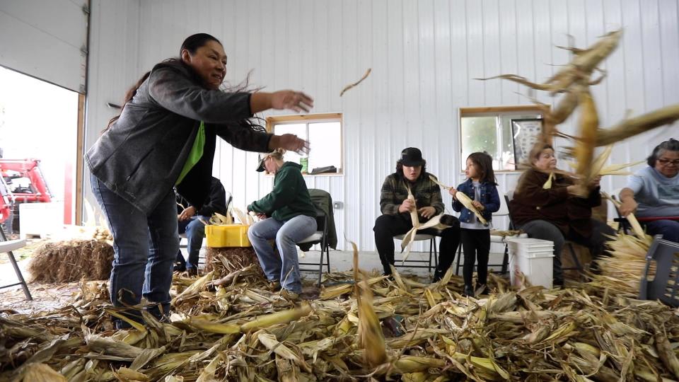 Gerry Fisher, acting director at Seneca Nation's Gakwi:yo:h Farms, laughs at a comment as she tosses corn to be husked to the other end of the circle.  "To me, without our corn, we'd be lost, our foods would be lost," she said.