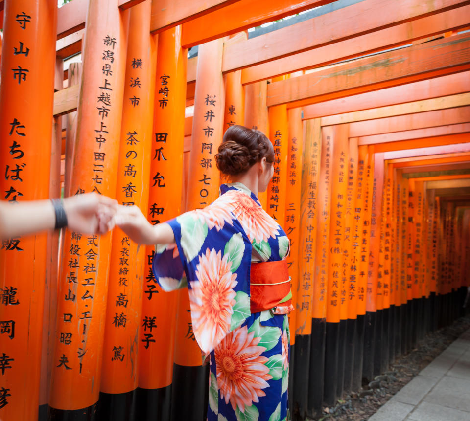 Kyoto, Japan - July 21, 2019: Young asian woman dressed in kimono walking under Senbon Torii gates in Fushimi Inari shrine