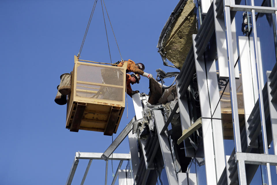 Workers suspended in a basket reach out toward debris from a building damaged when the crane atop it collapsed a day earlier, Sunday, April 28, 2019, in Seattle. The construction crane fell from a building on Google's new campus during a storm that brought wind gusts, crashing down onto one of the city's busiest streets and killing multiple people. (AP Photo/Elaine Thompson)