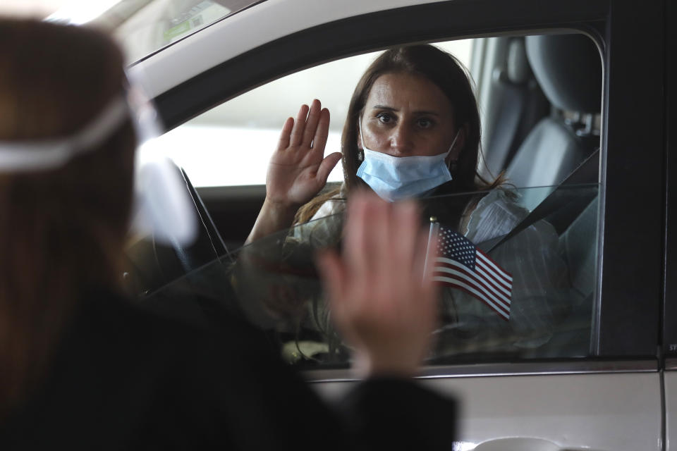 FILE- In this June 26, 2020, file photo, U.S. District Judge Laurie Michelson, left, administers the oath of citizenship to Hala Baqtar during a drive-thru naturalization service in a parking structure at the U.S. Citizenship and Immigration Services headquarters on Detroit's east side. U.S. Citizenship and Immigration Services has transformed under President Donald Trump to emphasize fraud detection, enforcement and vetting, which has delayed processing and contributed to severe fiscal problems. Its revamp came as the administration sought to cut legal immigration by making it more dependent on employment skills and wealth tests. (AP Photo/Carlos Osorio, FILE)