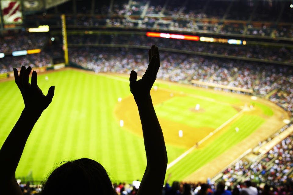 A fan high in the bleachers at a baseball stadium, silhouetted against the field