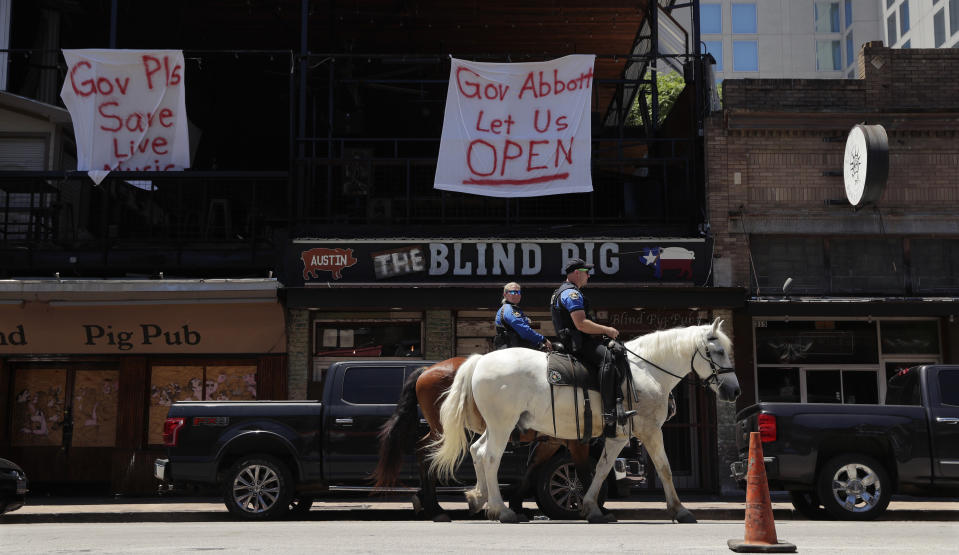 Austin police officers on horseback pass signs hanging on a pub directed at Texas Gov. Greg Abbott in Austin, Texas, Monday, May 18, 2020. Texas continues to go through phases as the state reopens after closing many non-essential businesses to help battle the spread of COVID-19. (AP Photo/Eric Gay)