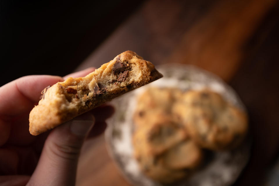 A hand holding a cookie with a bite out of it.