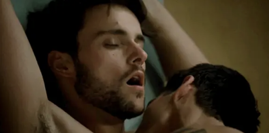 Two men engaged in an intimate moment, one with his eyes closed and mouth open, the other partially visible with his face close to the other's neck