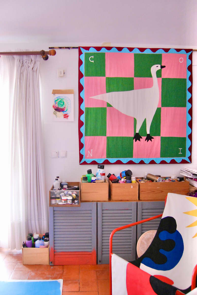 Boxes of paint on top of gray cabinets beneath colorful tapestry art.