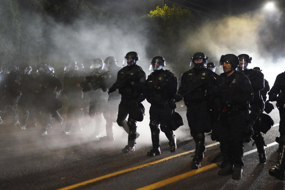 Portland police officers walk through the Laurelhurst neighborhood after dispersing protesters from Multnomah County Sheriff's Office early in the morning on Saturday, Aug. 8, 2020 in Portland, Ore. (AP Photo/Nathan Howard)