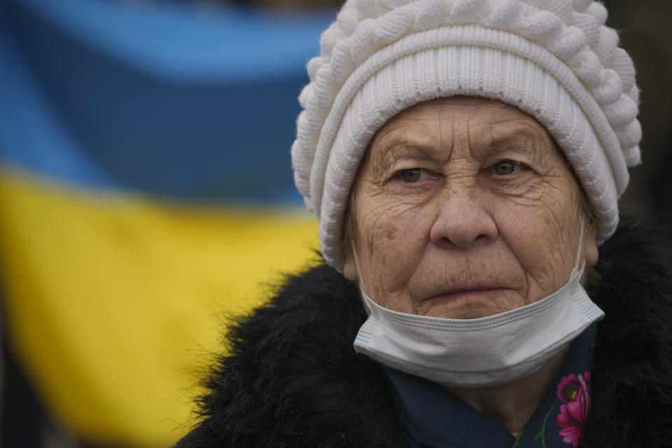 An elderly lady looks at people carrying a large Ukrainian flag as they mark a "day of unity" in Sievierodonetsk, the Luhansk region, eastern Ukraine, Wednesday, Feb. 16, 2022. The flags celebrated survival, endurance and above all, defiance. One blue and yellow banner curved along the edge of a stadium field. Others were tiny handheld things. One made it on the Olympic podium. Ukraine's president declared Wednesday a day of national unity in the face of “hybrid threats.” (AP Photo/Vadim Ghirda)