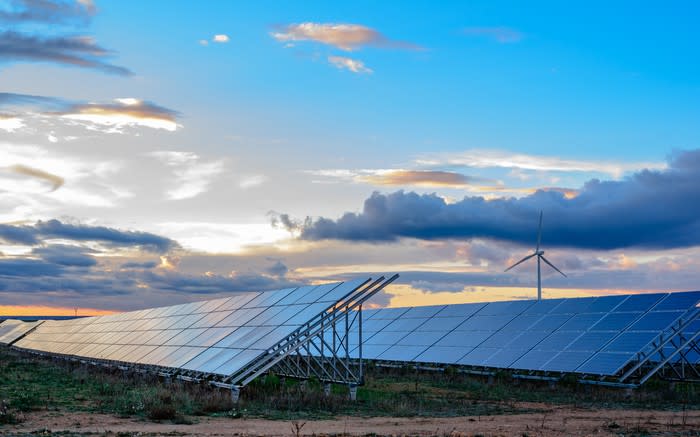 Solar panels and a wind turbine at dusk.