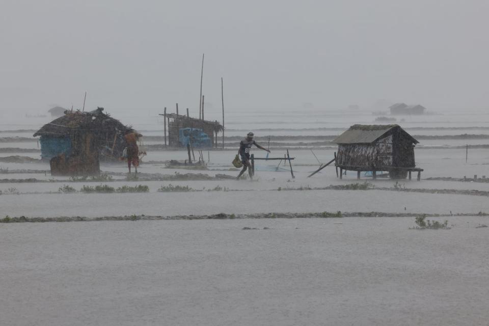 People walk along flooded shrimp and crab farms due to heavy rain as Cyclone Remal passes the country in the Shyamnagar area of Satkhira (Reuters)