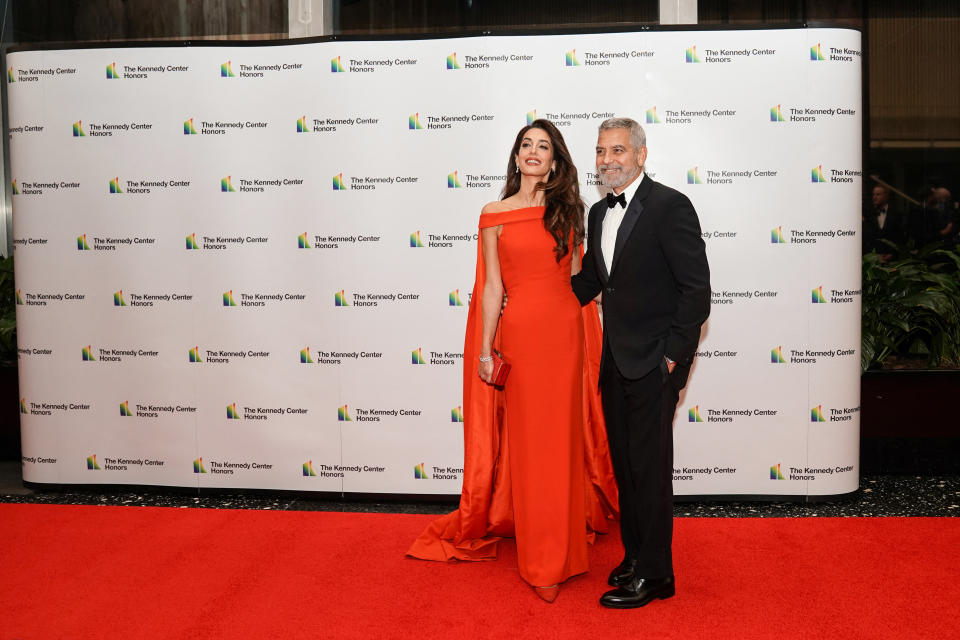 Amal Clooney wears a red Valentino gown as she poses next to husband George Clooney who wears a black tuxedo. (Reuters)