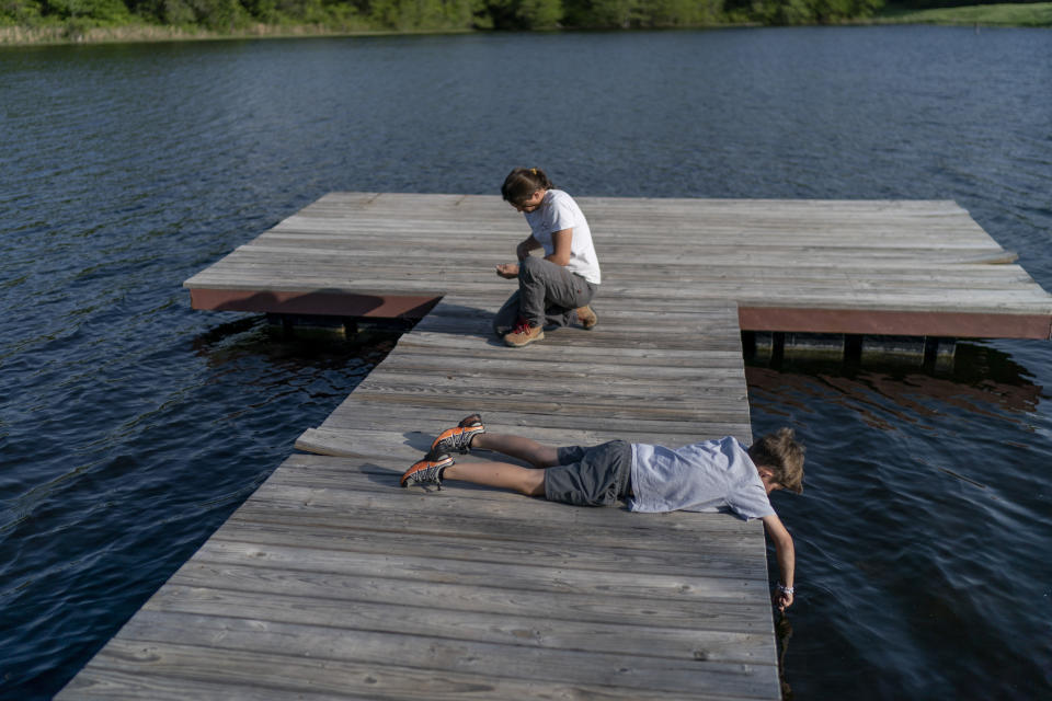 Rancher Meredith Ellis, right, fixes a fishing rod for her son, GC, 6, on their dock in Rosston, Texas, Thursday, April 20, 2023. Her parents built this ranch, and it's where Ellis was raised, roaming with her brother through the pastures, creeks and hardwood forests as the family added land and cattle over the years. (AP Photo/David Goldman)