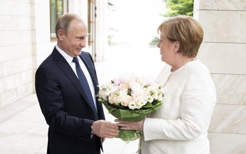 German Chancellor Angela Merkel is handed over a bouquet of flowers as she meets Russian President Vladimir Putin - Credit: Getty Images Europe