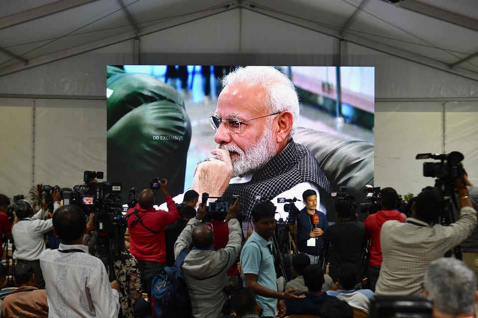 Members of the media cover the development as India's Prime Minister Narendra Modi is seen on a tv.