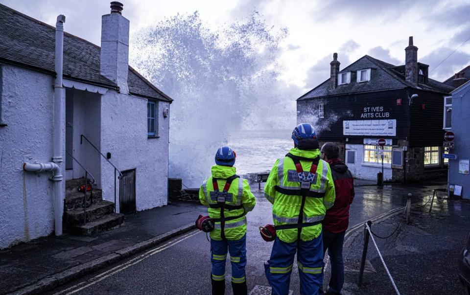 Coastguard personnel look on as waves crash over the harbour wall at St Ives, Cornwall