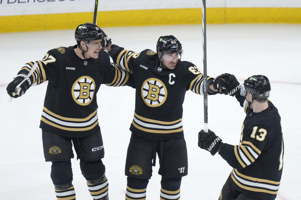 Boston Bruins left wing Brad Marchand (63) celebrates with defenseman Hampus Lindholm (27) and center Charlie Coyle (13) after scoring against the Vancouver Canucks during the first period of an NHL hockey game Thursday, Feb. 8, 2024, in Boston. (AP Photo/Steven Senne)