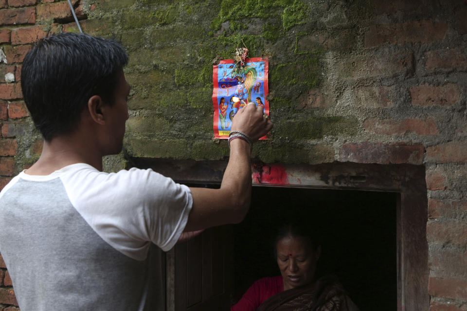 In this Aug. 5, 2019, photo, a Nepalese man displays a machine made painting on his house door during Naag Panchami festival in Bhaktapur, Nepal. The art and tradition of Nepal’s Chitrakar families, who depicted gods and goddesses on temples, masks of Hindu deities and posters for various religious celebrations is dying because of mass machine printed posters and card-size pictures of gods that are cheaper and more popular. (AP Photo/Niranjan Shrestha)
