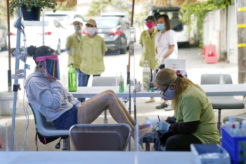 FILE - In this July 22, 2020, file photo, Tyson Salomon, left, gets a pedicure outside Pampered Hands nail salon in Los Angeles. Gov. Gavin Newsom announced a new, color-coded process Friday, Aug. 28, 2020, for reopening California businesses amid the coronovirus pandemic that is more gradual than the state's current rules to guard against loosening restrictions too soon. Counties will move through the new, four-tier system based on their number of cases and percentage of positive tests. It will rely on those two metrics to determine a tier: case rates and the percentage of positive tests. (AP Photo/Ashley Landis, File)