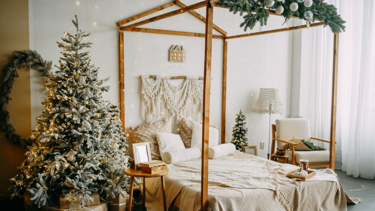  Image shows a green christmas tree with bright lights in a cozy bedroom decorated for the holidays. 