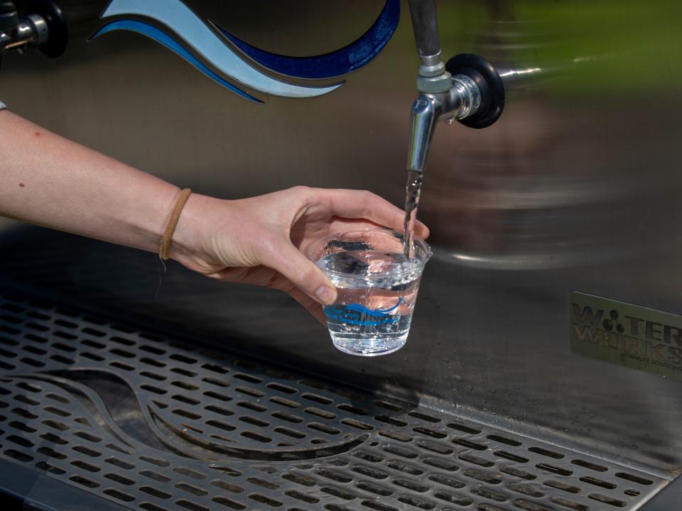 A photograph of a person getting water from a tap at a promotional event for the Bud Lewis desalination plant.